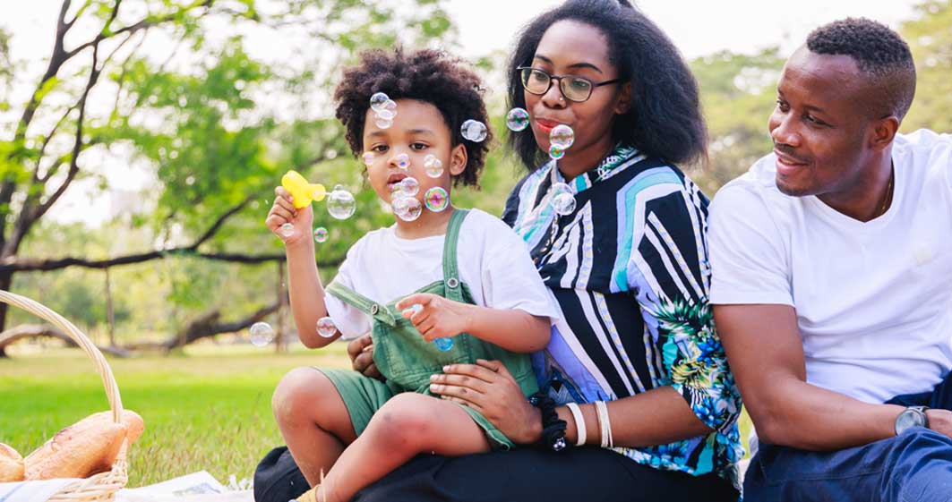 Family with baby blowing bubbles in the park.